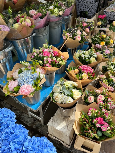 An array of freshly cut floral arrangements displayed on a table at a florist shop. The bouquets feature pink, white, and light purple roses, hydrangeas, and various greenery, wrapped in brown craft p